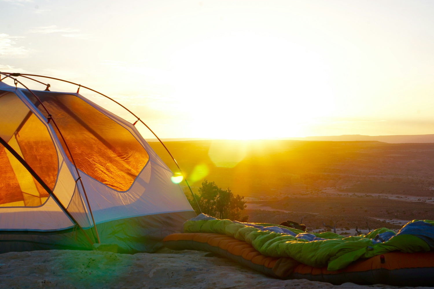 Camping tent pitched on a cliff edge at golden hour above a wide valley