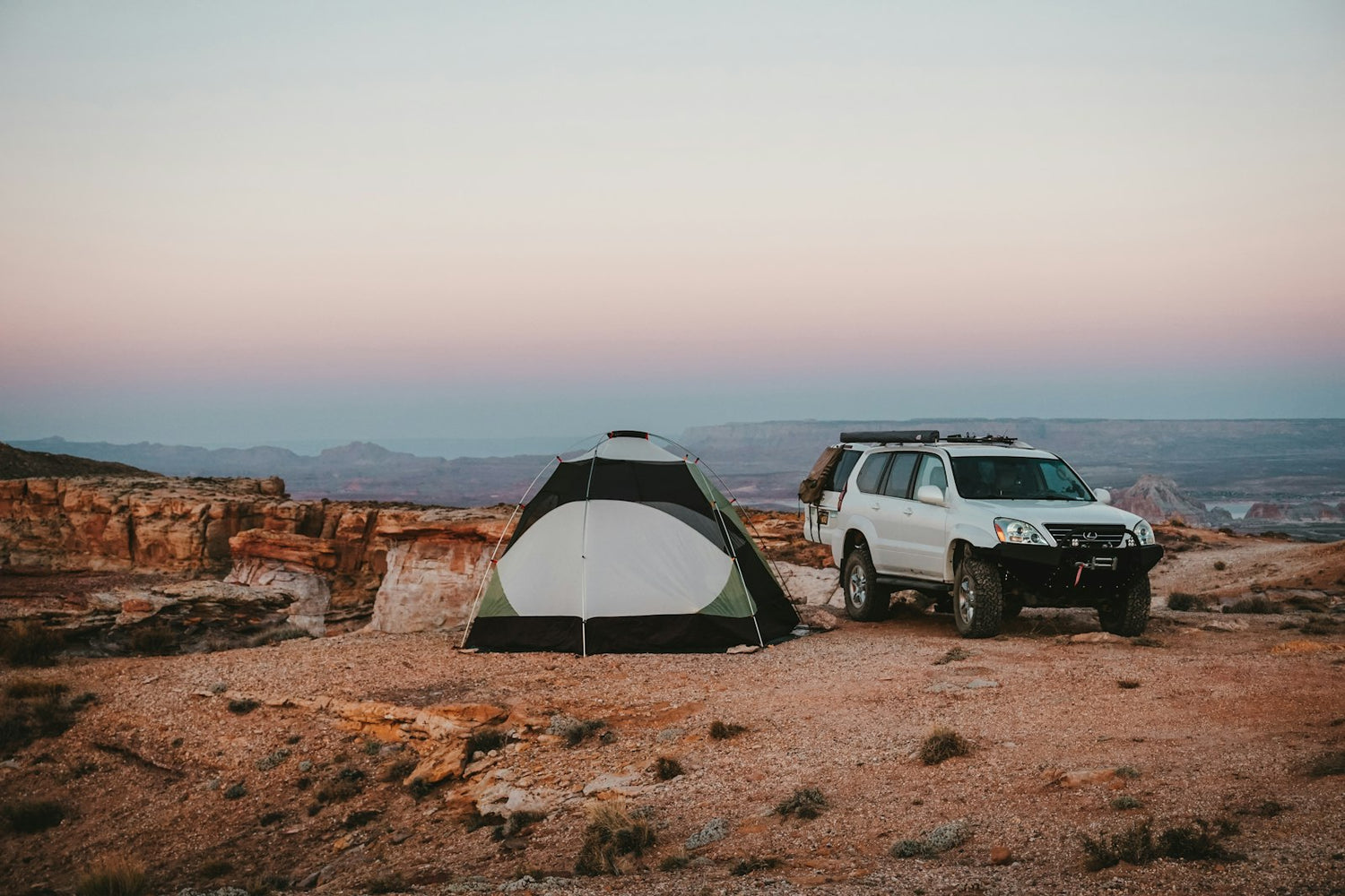 SUV parked beside a tent on a red sandstone overlook at a car camping site