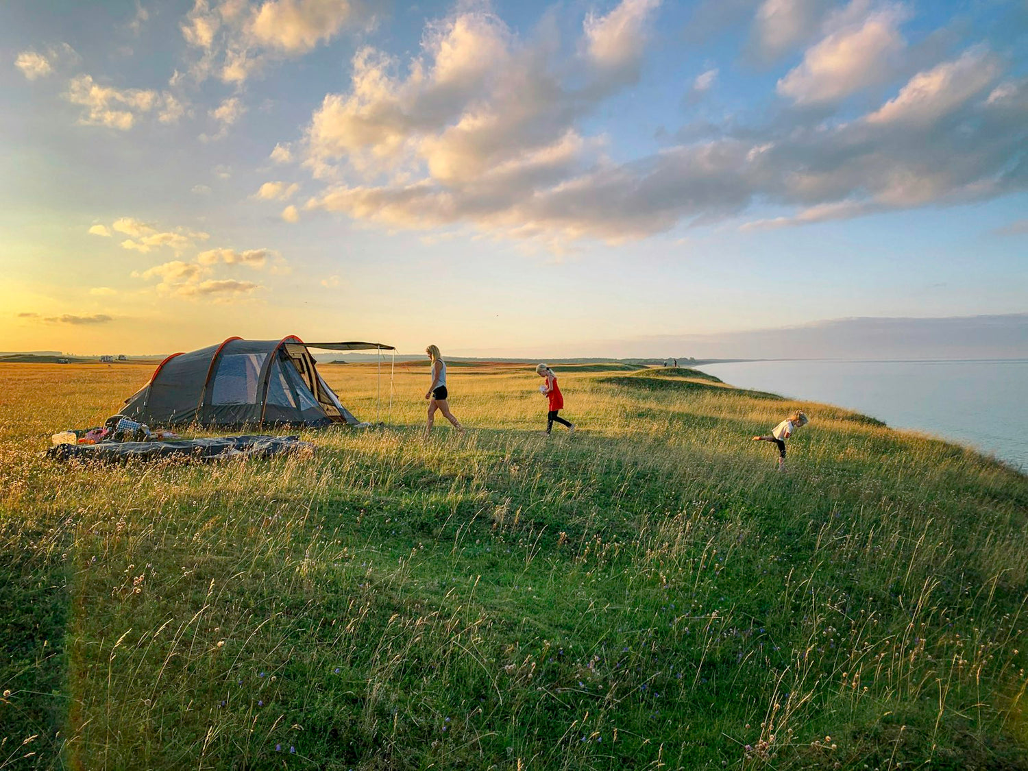 Young child walking on grass beside a pitched family tent at golden hour