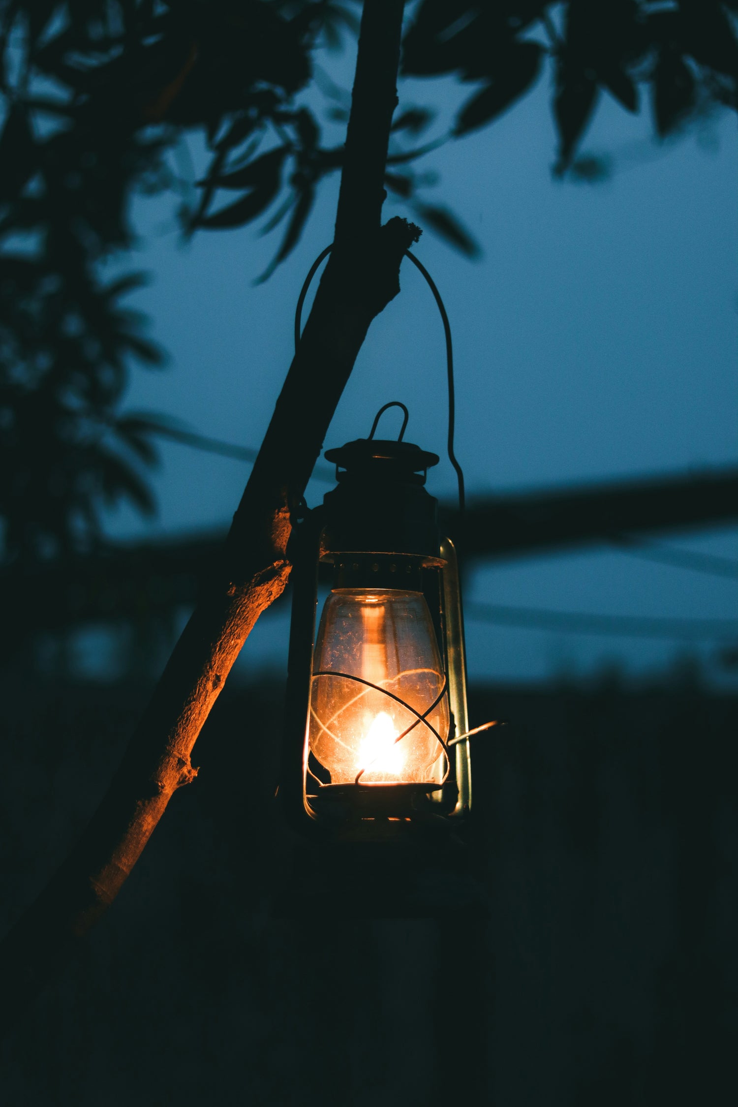 Lit camping lantern hanging in the dark at a campsite