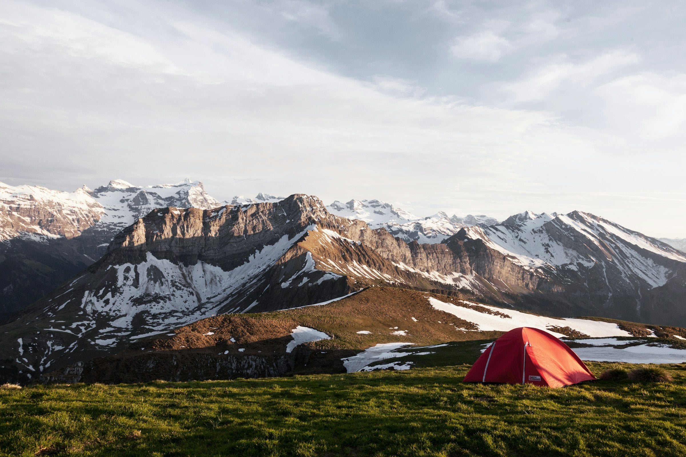 Red tent pitched in a mountain valley at golden hour